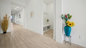 A hallway with wooden flooring, white walls, and a blue vase with flowers. - Modern Suburban Retreat Near Shopping & Parks (Manvel)