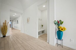 Un couloir doté d’un plancher en bois, de murs blancs et d’un vase bleu contenant des fleurs.