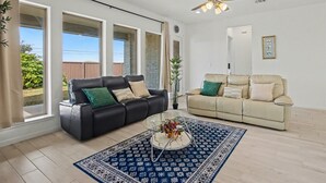 A spacious living room with two sofas, a coffee table, and a ceiling fan. - Modern Suburban Retreat Near Shopping & Parks (Manvel)