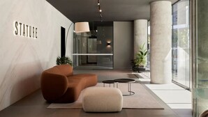 Een moderne lobby met een bank, voetenbankje en een glazen wand waarop het woord 'STATUE' staat.