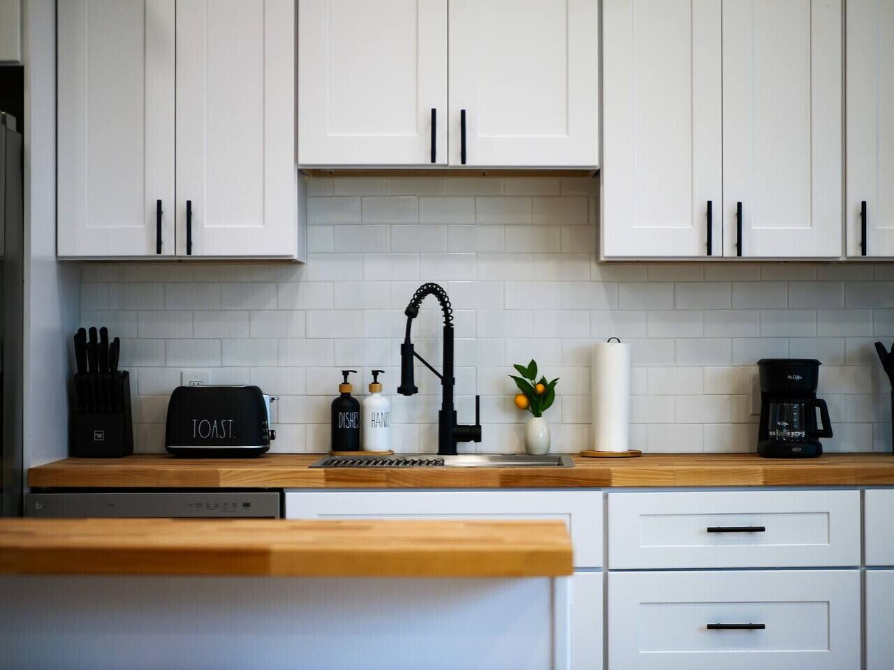 A modern kitchen with white cabinets, a black faucet, a toaster, and a coffee maker on the countertop.