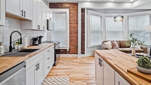 Une cuisine moderne avec des armoires blanches, un plan de travail en bois et un mur d’accent en briques.