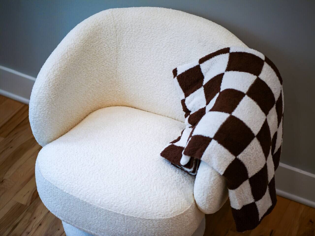 Un fauteuil blanc sur lequel est posé un plaid à carreaux.