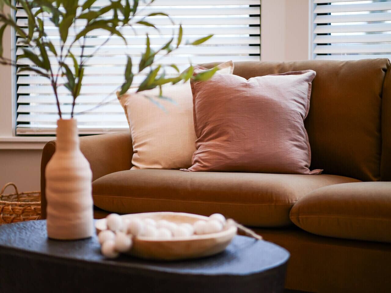 Un salon chaleureux avec un canapé marron, un vase rempli de petits galets blancs et un bol en bois posé sur une table d’appoint.