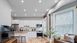 Une cuisine moderne avec des meubles blancs, un îlot central et un coin repas comprenant une table en bois et des tabourets de bar.