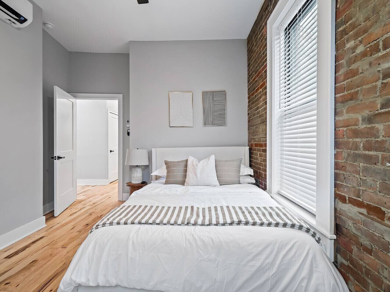 A bedroom with a bed, a nightstand, a lamp, and a window with blinds.