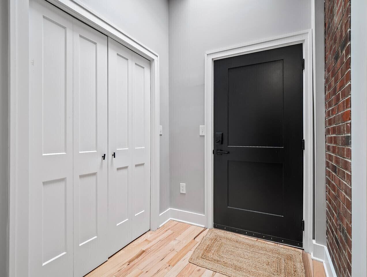 A hallway with a white door and a black door, a wooden floor, and a small rug.