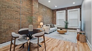 Ein modernes Wohnzimmer mit Backsteinwand, einem runden Esstisch mit Stühlen, einer Couch und einem Couchtisch.