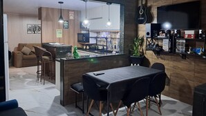 Et moderne køkken med spiseplads, der inkluderer en køkkenø, barstole og et TV ophængt på væggen.