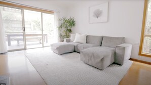 Una sala moderna con un sofá seccional, una planta grande en maceta y un ventanal corredizo que da a un espacio exterior.