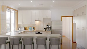 Una cocina moderna con armarios blancos, una isla central con taburetes y una máquina de espresso integrada.