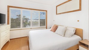 Un dormitorio con cama, televisor, cómoda y ventana con persianas.