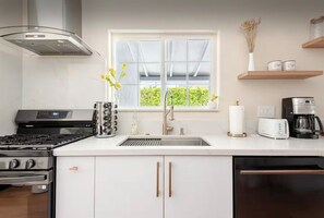 Una cocina moderna con estufa a gas, electrodomésticos de acero inoxidable, un ventanal con vistas a zonas verdes y una encimera blanca.