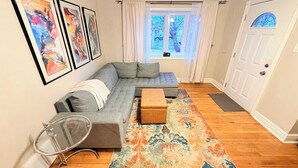 A living room with a sectional sofa, a glass coffee table, a patterned rug, and artwork on the wall. - Furnished monthly rental Near Downtown Denver (Denver)