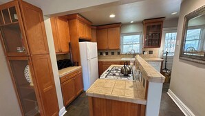 A kitchen with wooden cabinets, a white refrigerator, a gas stove, and a window with a view of the outside. - Furnished monthly rental Near Downtown Denver (Denver)
