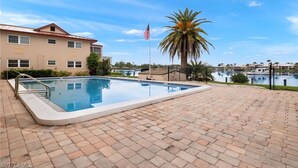 Ein Pool mit Metallleiter, einer Palme und Blick auf ein Gewässer mit Gebäuden im Hintergrund.