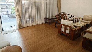 A living room with a wooden floor, a sofa, a coffee table, and a dining table with chairs. There is a window with curtains, and an air conditioning unit on the wall. - Holiday Home Bali (Denpasar)
