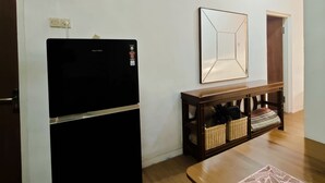 A room with a black refrigerator, a wooden table with a decorative mat, a small wooden console table with baskets, and a framed picture on the wall. - Holiday Home Bali (Denpasar)
