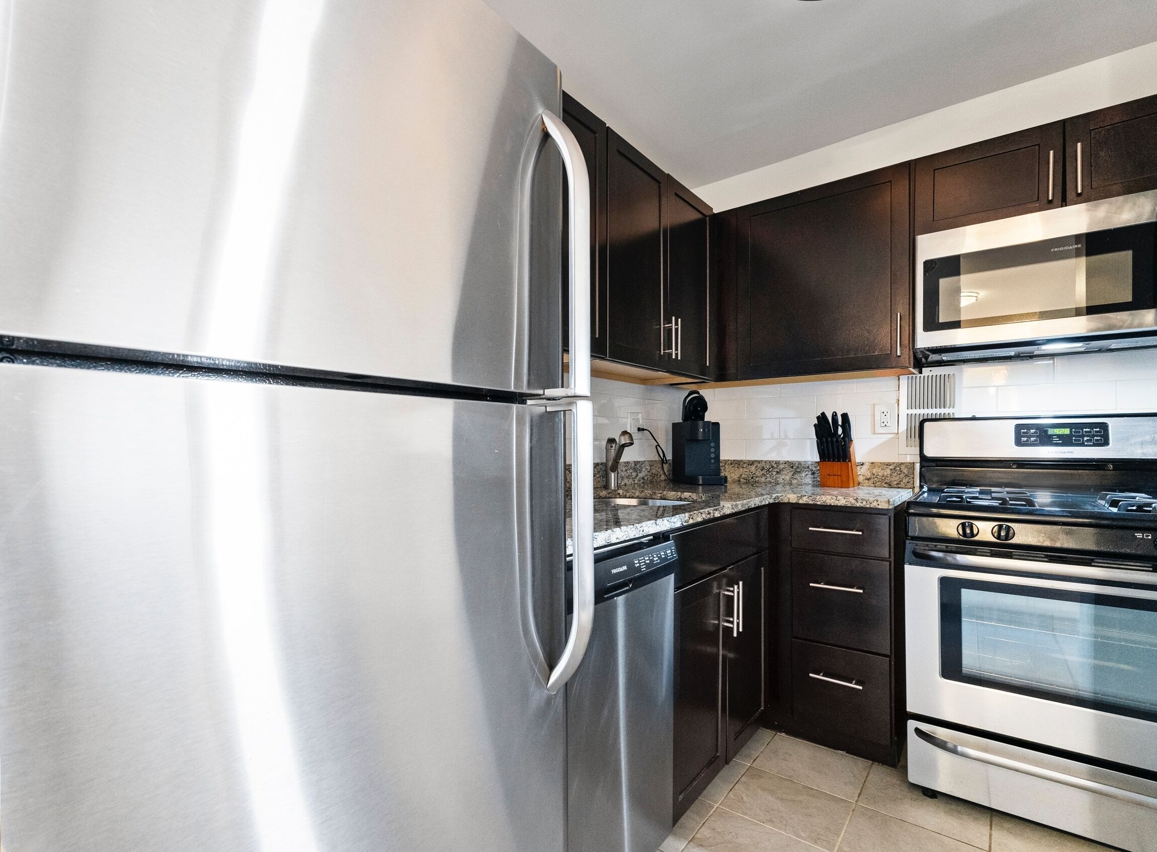 A modern kitchen with stainless steel appliances, dark wooden cabinets, and a granite countertop.