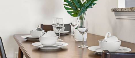 A dining table set with white dishes, glasses, and a potted plant.