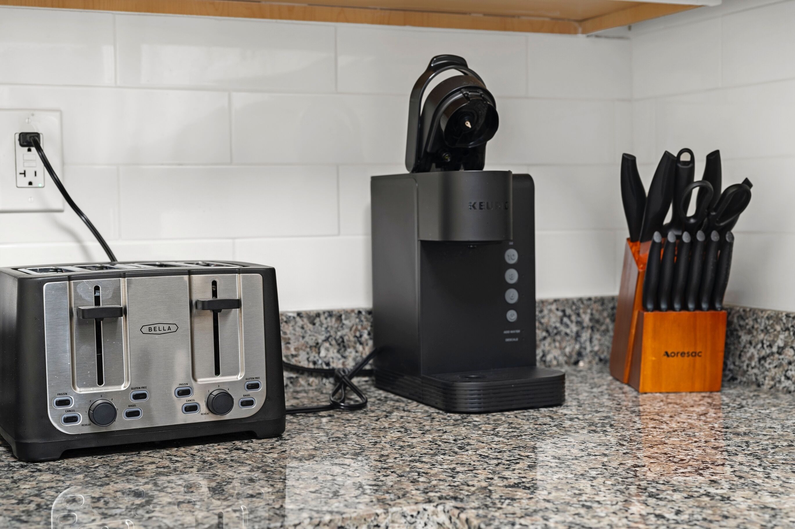 Una cocina con un tostador, una cafetera y un organizador de cuchillos sobre una encimera de granito.