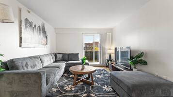 Een moderne woonkamer met een grijze modulaire bank, een ronde salontafel en een kamerkleed met een patroon.