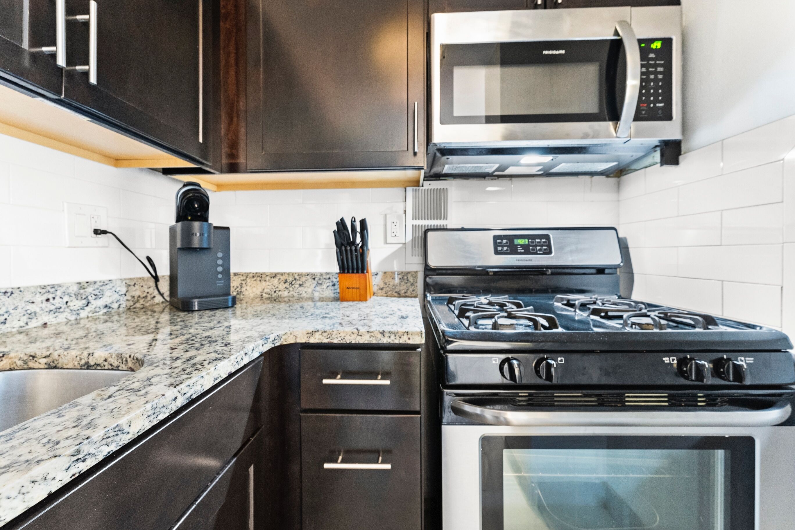 A modern kitchen with stainless steel appliances, granite countertops, and dark cabinetry.