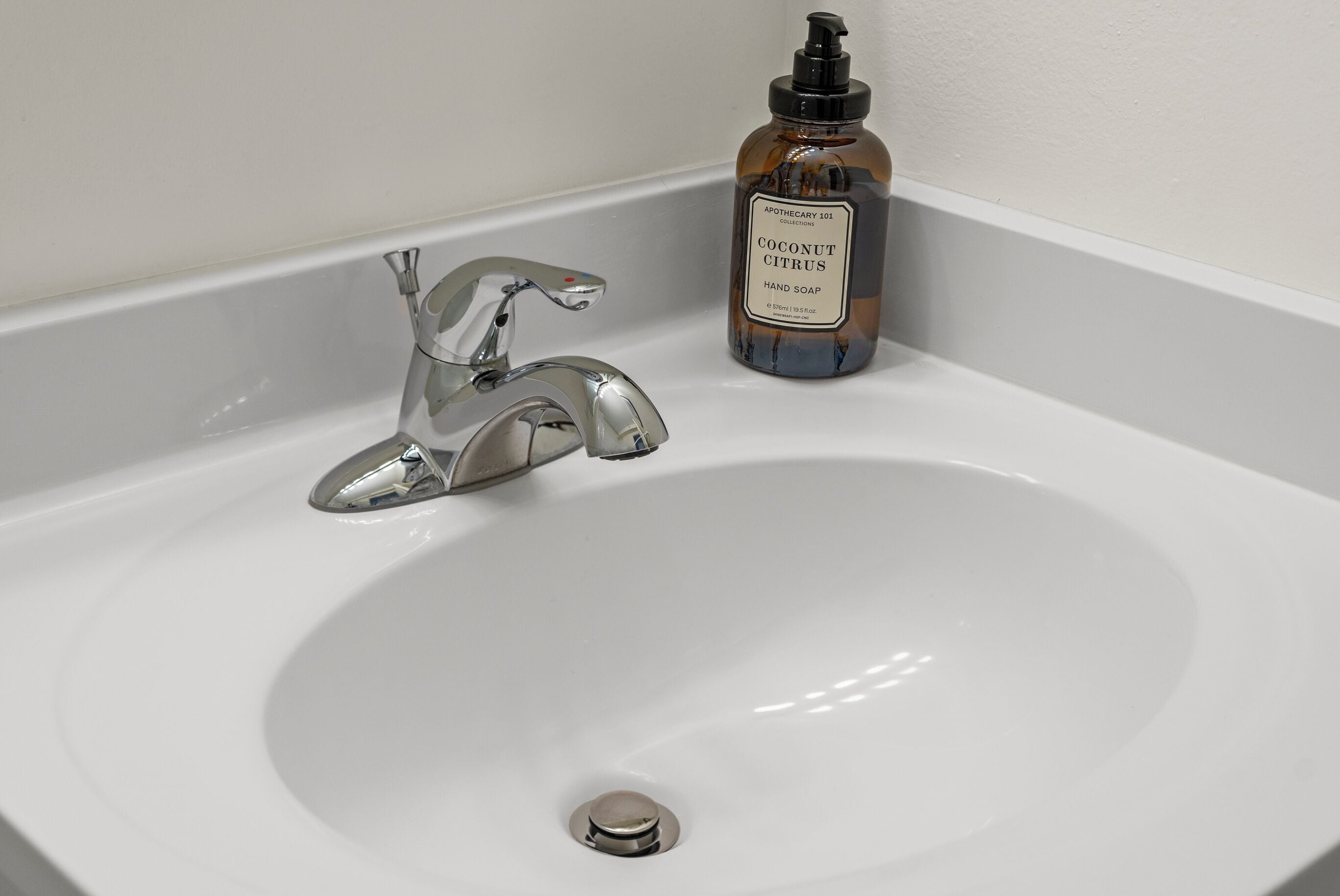 A white sink with a chrome faucet and a bottle of hand soap labeled "Coconut Citrus" on the side.
