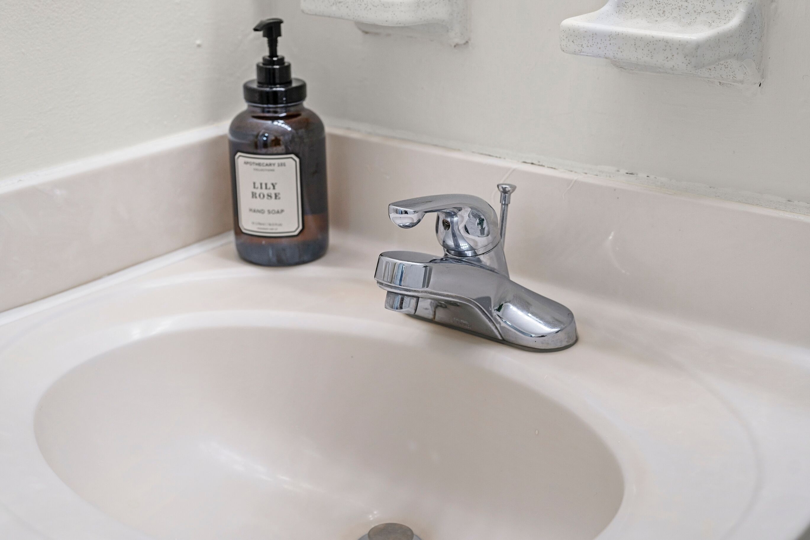 A bathroom sink with a chrome faucet and a bottle of hand soap.