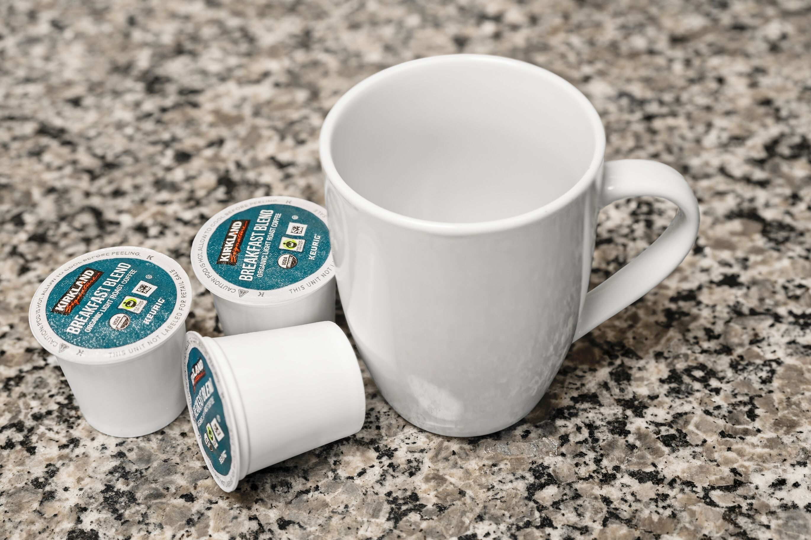 Eine weiße Tasse und drei Kaffeekapseln auf einer Granitarbeitsplatte.