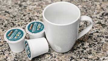Eine weiße Tasse und drei Kaffeekapseln auf einer Granitarbeitsplatte.
