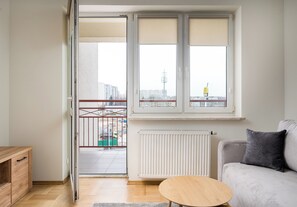 A room with a sliding glass door leading to a balcony, a white radiator, a grey sofa, and a wooden table. - Bemowo Spacious Apartment (Warszawa)
