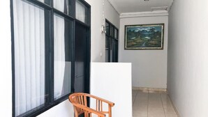 A narrow hallway with a wooden chair and a table, a painting on the wall, and large windows with black frames. - Cahaya Adrian Near Komodo Airport (Labuan Bajo)
