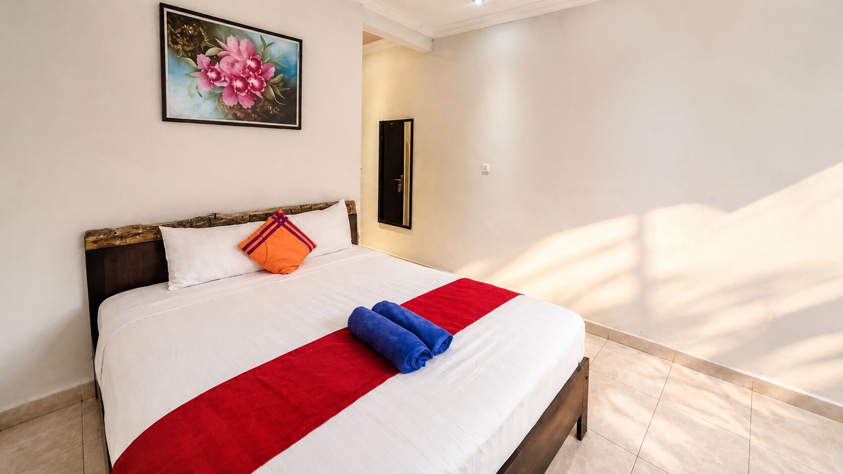A neatly made bed with a red and white bedspread, a pillow, and rolled towels.