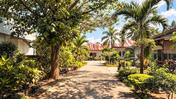 A pathway leading to a building with a red roof, surrounded by lush greenery and palm trees. - Cahaya Adrian Near Komodo Airport (Labuan Bajo)