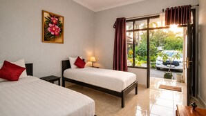 A hotel room with two beds, a nightstand, a lamp, a window with curtains, and a view of the outside. - Cahaya Adrian Near Komodo Airport (Labuan Bajo)
