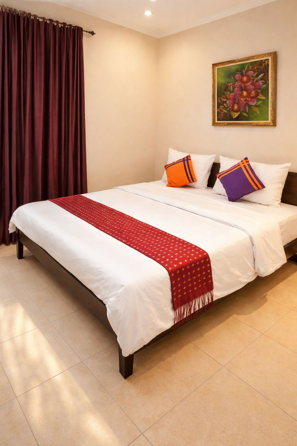 A hotel room with a bed, curtains, a painting, and a red and white bedspread.