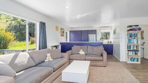 A modern living room with a sofa, a coffee table, and a bookshelf. - Kuaotunu Vista - Ocean Views (Kuaotunu)