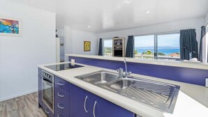 A modern kitchen with a large window, a built-in oven, and a view of the sea. - Kuaotunu Vista - Ocean Views (Kuaotunu)