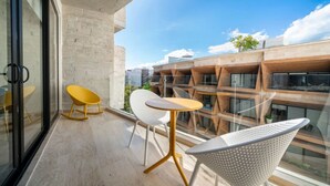 Ein Balkon mit zwei Stühlen und einem Tisch, eine Betonwand und Blick auf ein Gebäude mit hölzernen Balkonen.