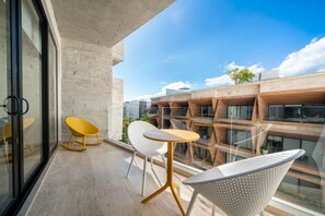 A balcony with two chairs and a table, a concrete wall, and a view of a building with wooden balconies. - Luxury Studio | Gym, Co-Work, Rooftop Pool & Beach (Playa del Carmen)