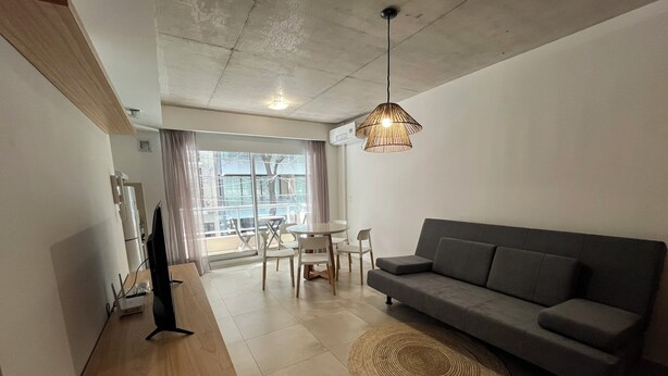 A modern living room with a grey sofa, a wooden coffee table, a woven rug, and a dining area with a table and chairs. - Rent Up - Dpto luminoso en Recoleta (Buenos Aires)
