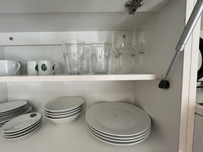 Une étagère de cuisine avec des assiettes blanches empilées et de la verrerie transparente.