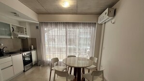 A compact kitchen with a stove, sink, and cabinets, a dining table with chairs, and a large window with sheer curtains. - Rent Up - Dpto luminoso en Recoleta (Buenos Aires)