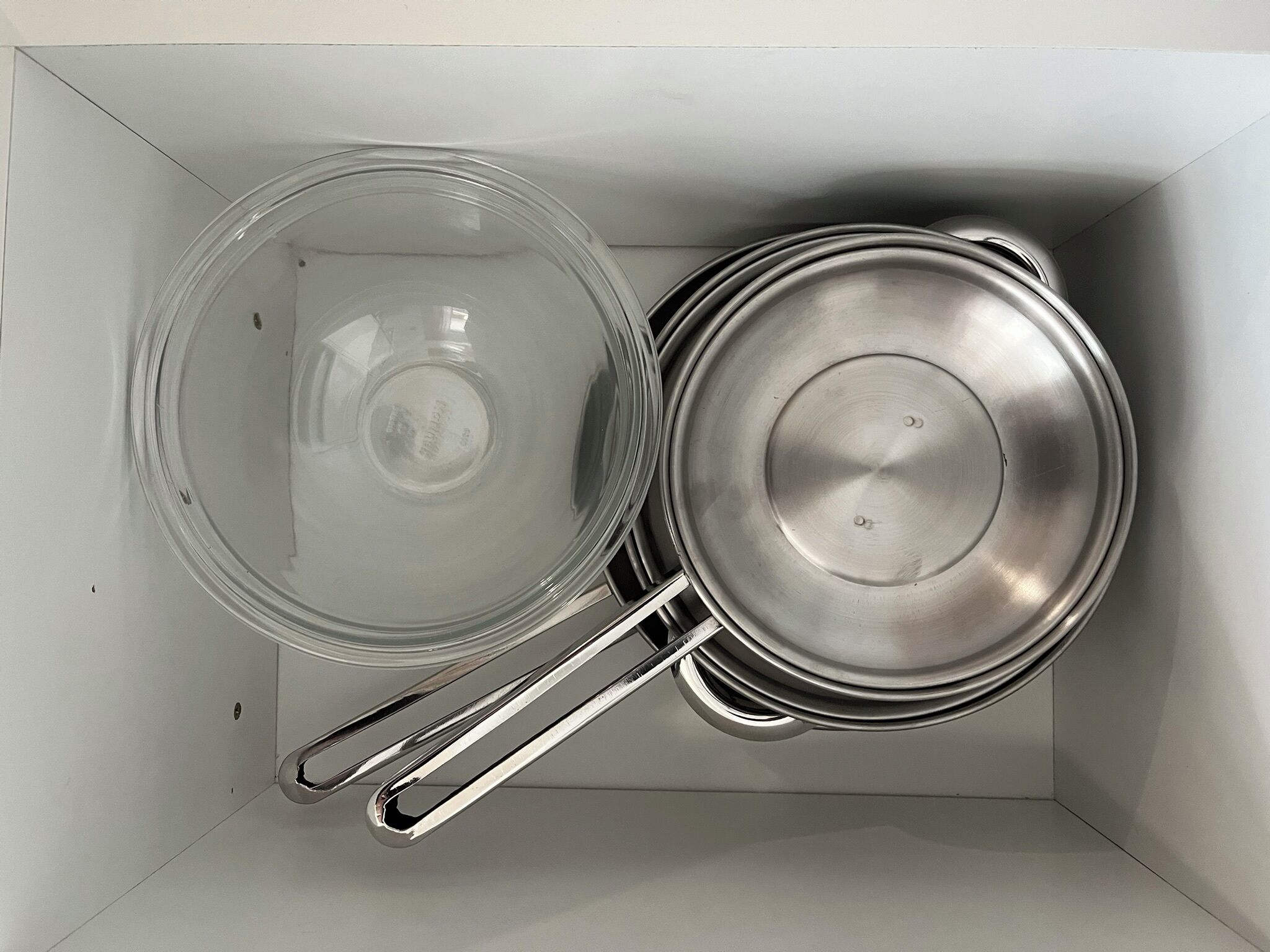 Eine Küche mit Edelstahlkochgeschirr, darunter ein Topf und eine Pfanne, in einem Schrank aufbewahrt.