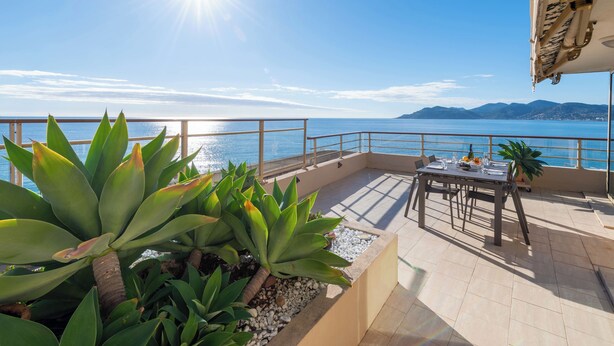 A terrace with a table set for dining, overlooking a body of water and distant mountains. - 2-Br Panoramic Sea View & Beach Access (Cannes)