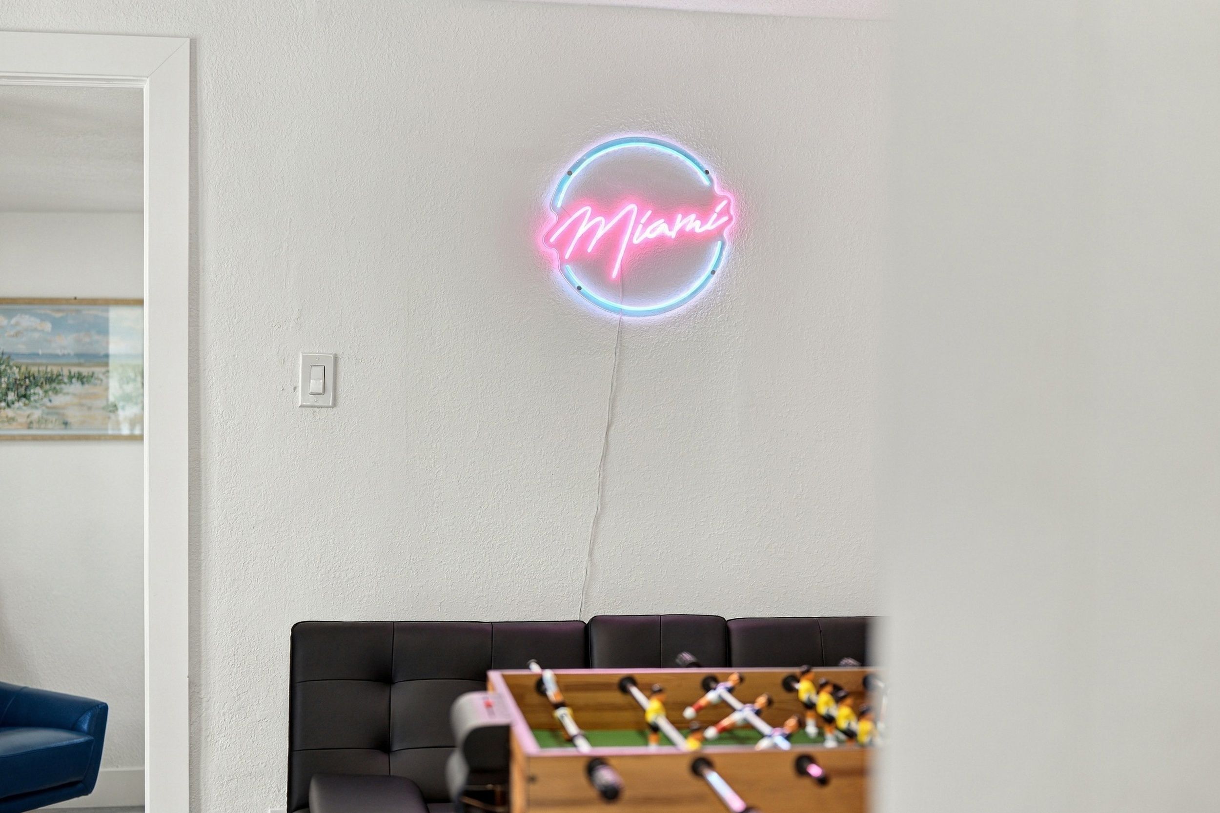 Une pièce avec un néon mural, un canapé et une table de baby-foot.
