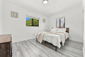 A bedroom with a bed, two windows, a bedside table, and a dresser.