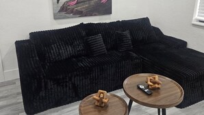 Uma sala de estar moderna com um sofá seccional preto, duas mesas de centro de madeira e uma pintura de um flamingo.