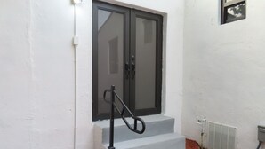 Fachada branca com porta escura, um pequeno lance de degraus de concreto e um corrimão de metal.
